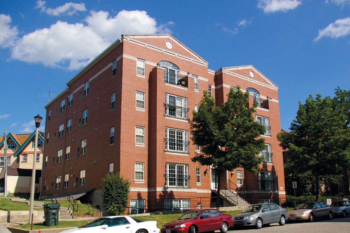 Red brick apartment building with multiple windows and balconies, under a blue sky.