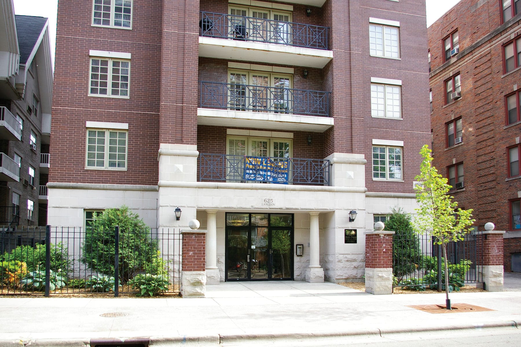 Brick apartment building entrance with balconies, windows, and a small tree.