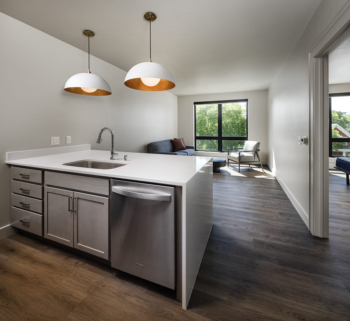 Modern kitchen island with sink and dishwasher, open to living area with sofa and chair.