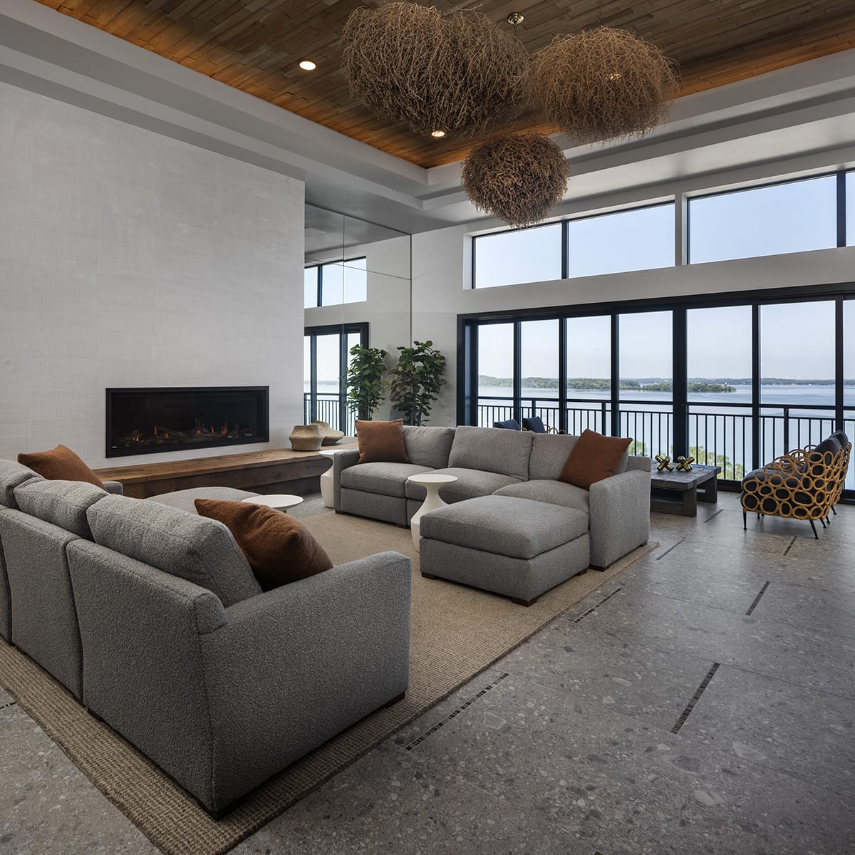 Modern living room with sectional sofa, fireplace, and large windows overlooking a lake.