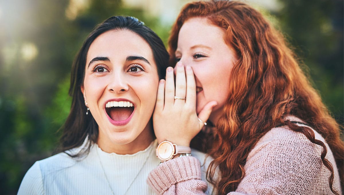 Photo of a young lady whispering in another young lady's ear
